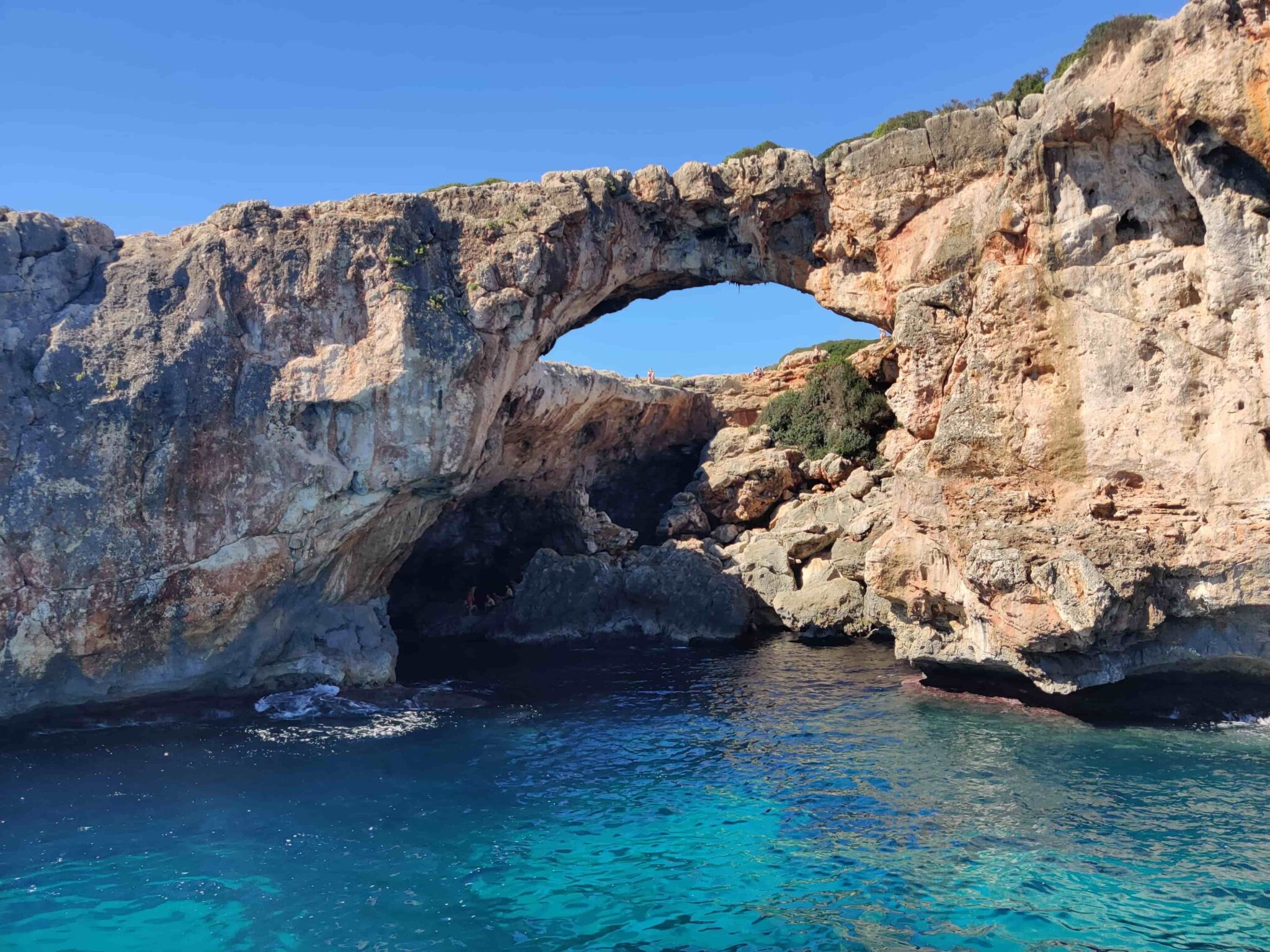 Crystal clear turquoise water at Cala Varques with limestone cliffs and pine trees, Mallorca