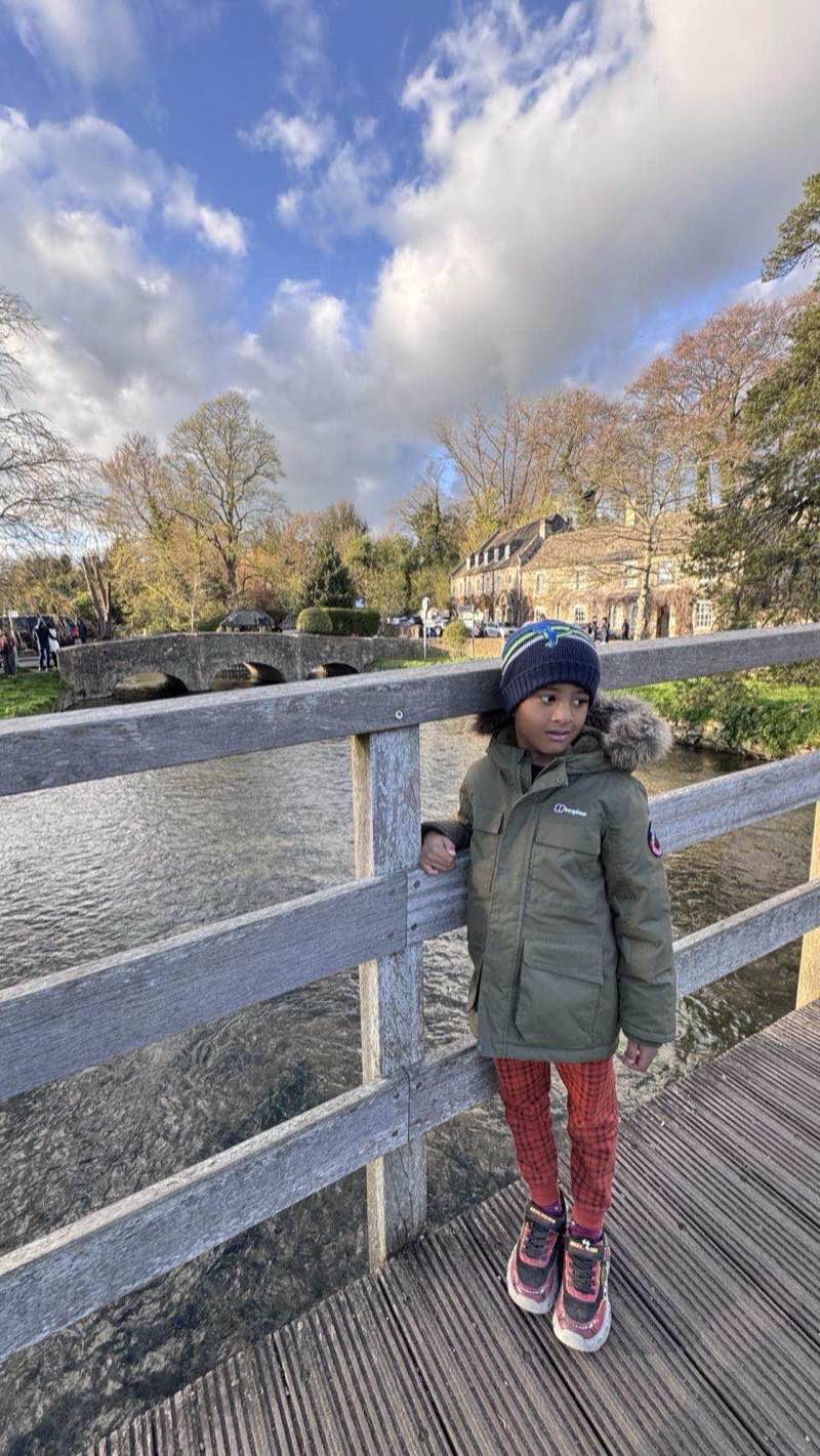 A child standing on the bridge over the River Coln in Bibury with stone cottages visible in the background