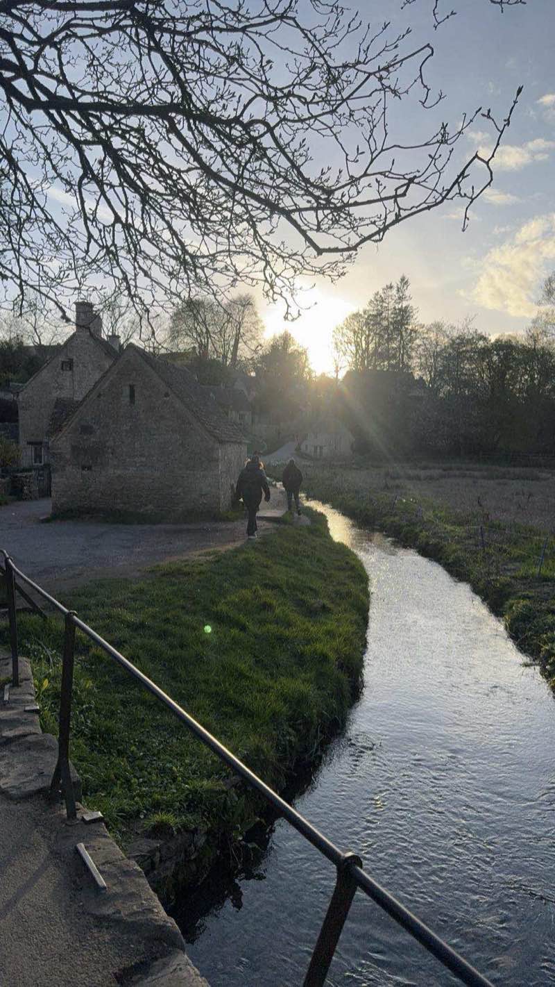 The River Coln at sunset in Bibury, with golden light on the water and stone buildings in the background